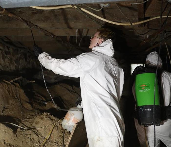 SERVPRO technician in a hazmat suit spraying chemicals underneath a house